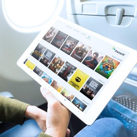 Close-up of a hand holding a tablet viewing movies inflight entertainment options on the Viasat portal
